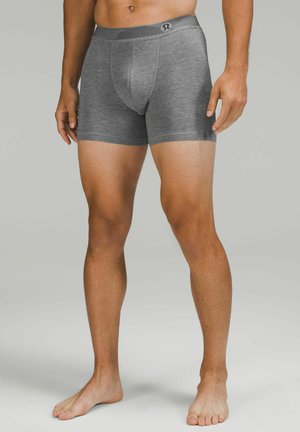 Pilki bokseriai su aptempiančiu prigludimu, pasižymintys struktūruota medžiaga ir juosmens logotipu. Dizainas iki vidurio šlaunies, pagamintas iš tamprios medžiagos.