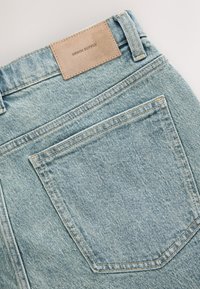 Lichtblauwe spijkerbroek met een bruin leren label met de tekst "DENIM SUPPLY", voorzien van een achterzak en contrasterende stiknaden.