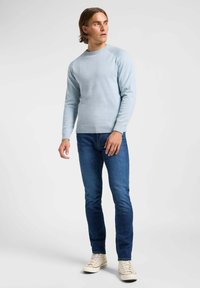  Lichtblauwe gebreide trui met een ronde hals, geribbelde mouwen en zoom, gedragen met donkerblauwe jeans en beige sneakers.