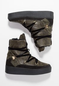 Baskets montantes en camouflage vert avec une tige en cuir texturé, accents en sue de noir, semelle en caoutchouc épaisse noire et détails en métal doré.