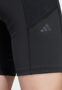 Shorts de sport noirs avec une texture lisse, dotés d'une poche en maille sur le côté et d'un subtil logo Adidas noir. Vue rapprochée des détails de couture.