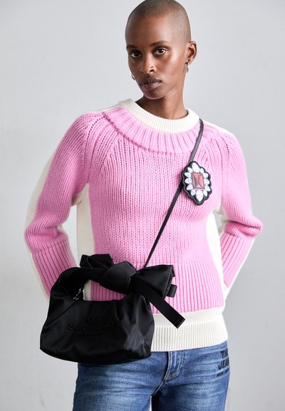 Suéter de punto rosa con textura acanalada y acentos en crema, combinado con un bolso de tela negro que presenta un lazo y texto en relieve.