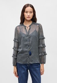 Μπλούζα με ναυτ ικό σχέδιο, διακοσμημένα διάφανα ρυάκια μανίκια, κουμπιά μπροστά και λεπτομέρεια με φούντα στον λαιμό. Απαλή υφή και ελαφρύ ύφασμα.