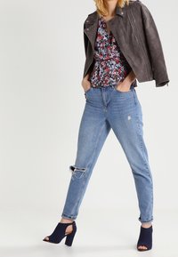 Giacca di pelle grigia, top con peplo floreale, jeans strappati azzurri e mule con tacco alto navy e punta aperta. Combinazione di outfit casual.