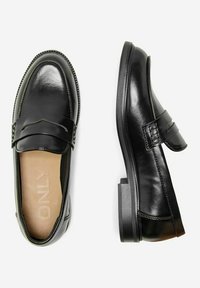 Mocasines de cuero negro con un acabado suave, que presentan un detalle frontal elevado, puntera redondeada y un tacón bajo y cuadrado. El interior muestra el logo de la marca.