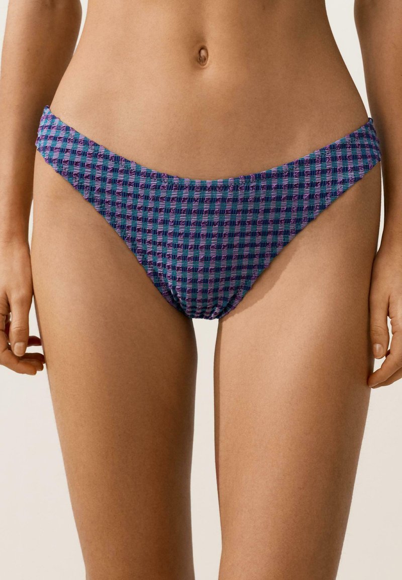 Kobieta ubrana w fioletowo-niebieskie bikini w kratkę z teksturowanym wzorem, widoczna od środka tułowia do górnej części ud.