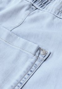 Tissu en denim bleu clair avec une texture lisse, présentant un petit bouton argenté et une couture jaune contrastante le long des coutures.