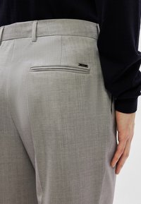 Calças cinzentas feitas à medida com um padrão texturizado subtil, apresentando um bolso traseiro com uma etiqueta da marca e um cós liso.