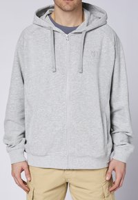 Gray zip-up hoodie with a textured finish, hood, drawstrings, and front pockets. Features a small logo on the chest and ribbed cuffs.