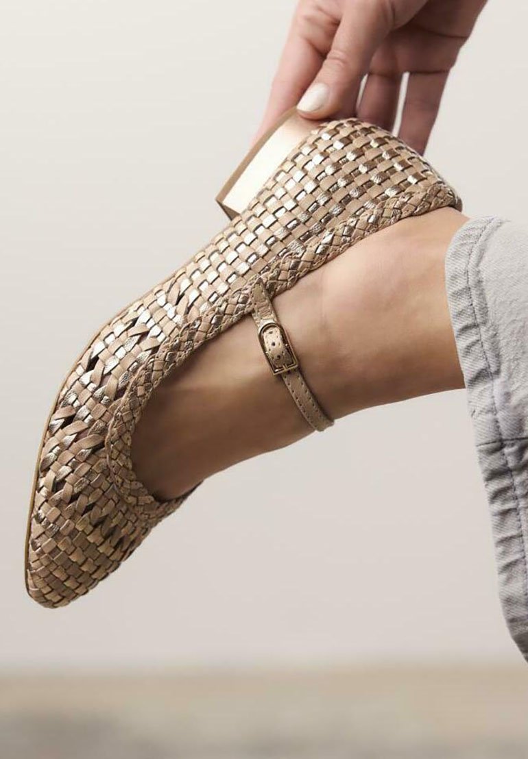 Zapato tejido beige con tacón bajo, tira en el tobillo y superficie texturada, con acentos metálicos y forma de punta curva.