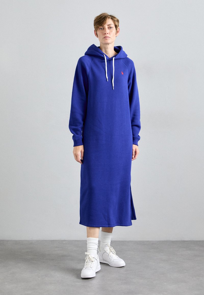 Hooded, garo piedurkņu kleita spilgti zilā kokvilnas audumā ar sānu šķēlumu, ar mazu sarkanu logotipu uz krūškurvja un baltām auklām.