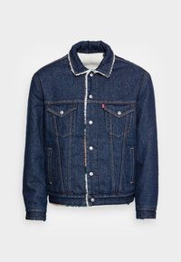 Denimjacka med mörkblå utsida, vit fleecefoder, spetsig krage, knappstängning och framfickor med lock och knapppdetaljer.