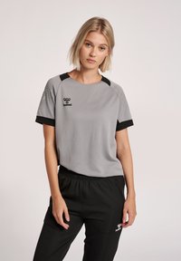 Grijze sportshirt met korte mouwen en zwarte accenten, met een textuurontwerp en logo op de borst. Gecombineerd met zwarte broek.