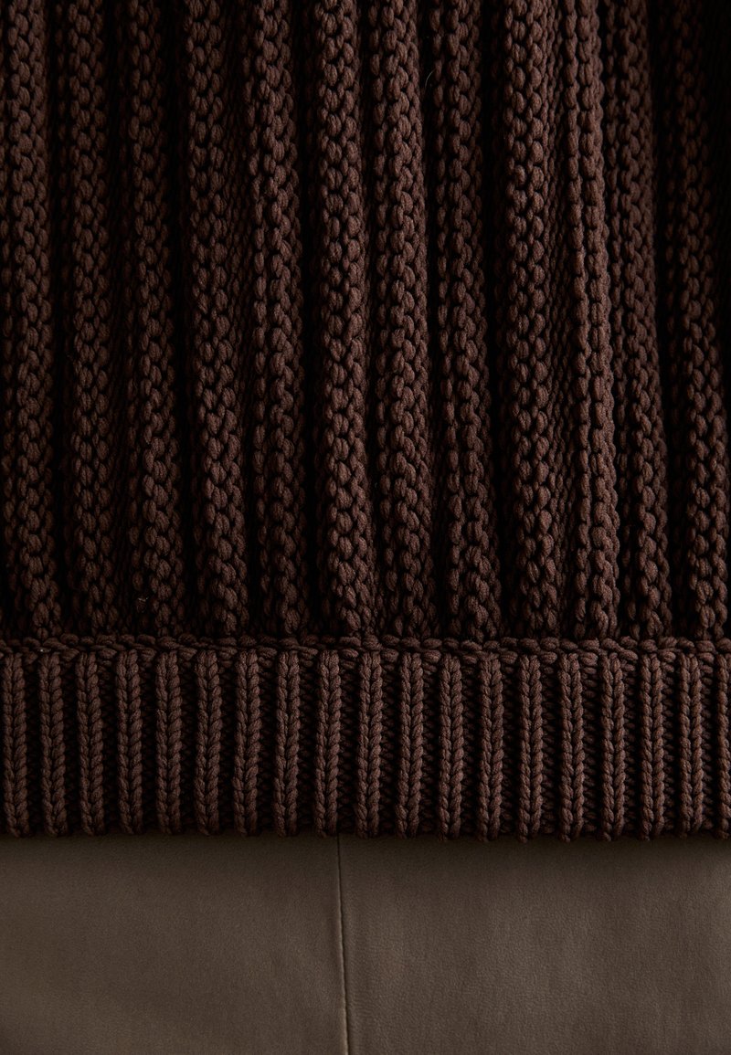 Knit brown sweater with vertical ribbing, featuring a textured fabric and a contrasting ribbed hem. Smooth surface underneath.