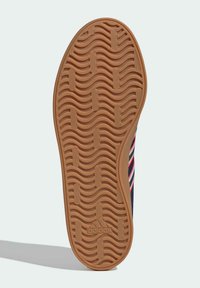 Adidas sneaker outsole, featuring a textured, wavy pattern in light brown rubber, with an embossed logo in the center.