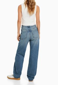 Jeans de tiro alto en azul claro con un corte holgado, que presentan grandes bolsillos traseros y una cinturilla lisa, combinados con zapatillas blancas.