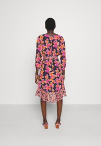 Vestido floral de manga larga en azul marino, con patrones de flores rosas y naranjas, cinturón en la cintura y dobladillo con volantes. Sandalias de tacón cuadrado de ante.