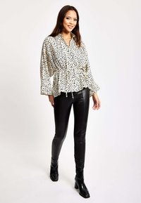 White shirt with black polka dots, long sleeves, cinched waist, paired with black fitted pants and ankle boots. Smooth texture and relaxed fit.
