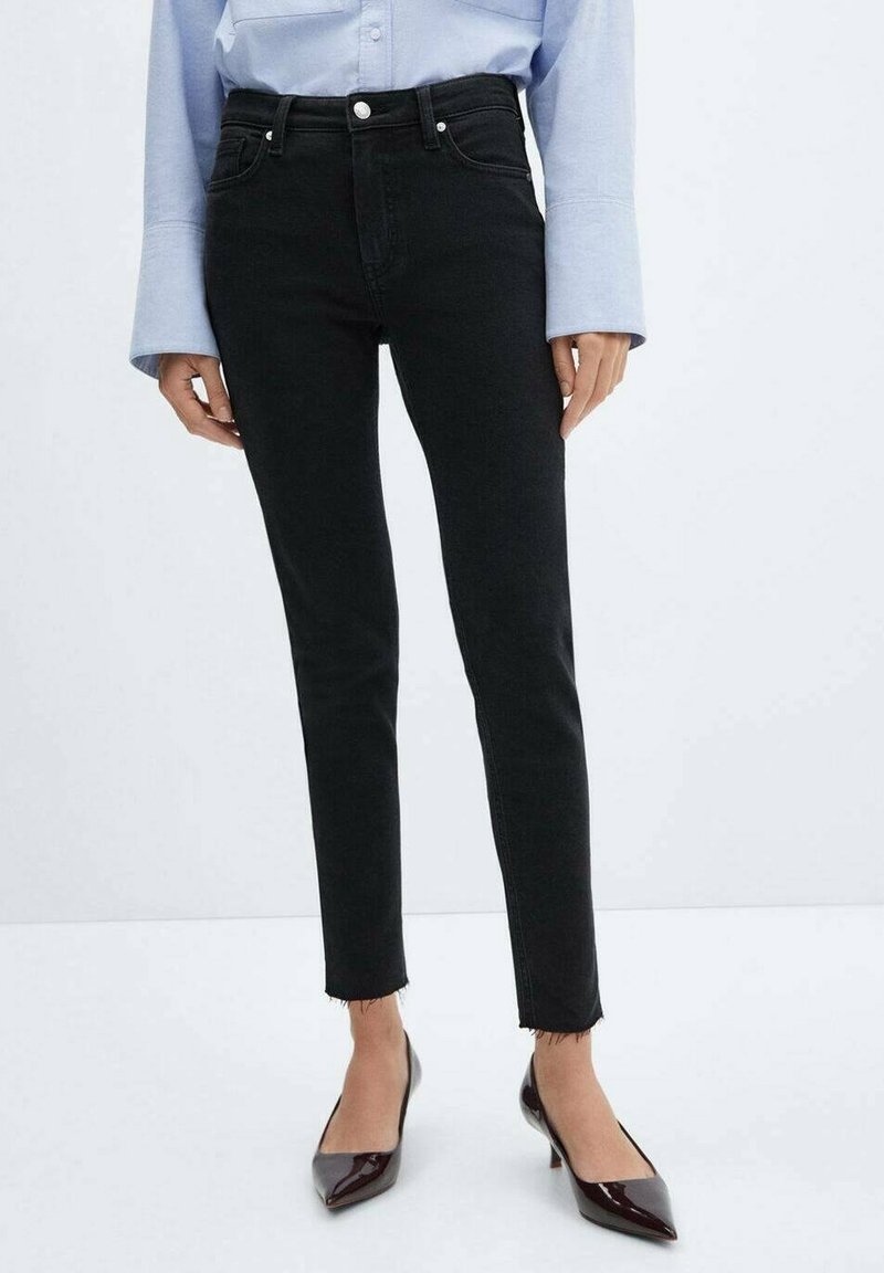 Jeans skinny negros con dobladillo deshilachado, cintura alta, diseño de cinco bolsillos y costura en contraste, combinados con tacones de punta.