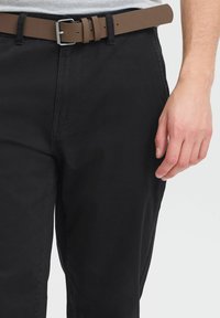Pantalon noir à coupe droite, avec une texture lisse, associé à une ceinture marron avec une boucle en métal argenté.
