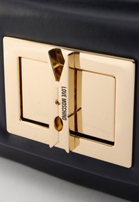Navy textured handbag featuring a gold metal clasp with a decorative clip design, engraved with "LOVE MOSCHINO".