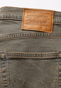 Poche arrière d’un jean en denim bleu avec une étiquette en cuir marron Levi Strauss & Co. cousue au-dessus de la poche.