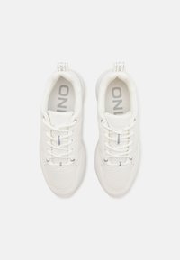 Weiße Sportschuhe mit Mesh-Details, runder Zehenpartie, Schnürdesign und Logo auf der Innensohle und am Fersenbereich. Glatte Textur und abgerundete Sohle.