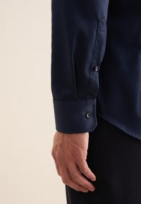 Marineblauwe longsleeve shirt met een gladde textuur, voorzien van knoopmanchetten en een subtiele geborduurde detail nabij de manchetten.