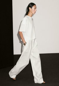 Volný bílý crop top a široké kalhoty z lehkého materiálu, s minimalistickým designem a texturovanými detaily.