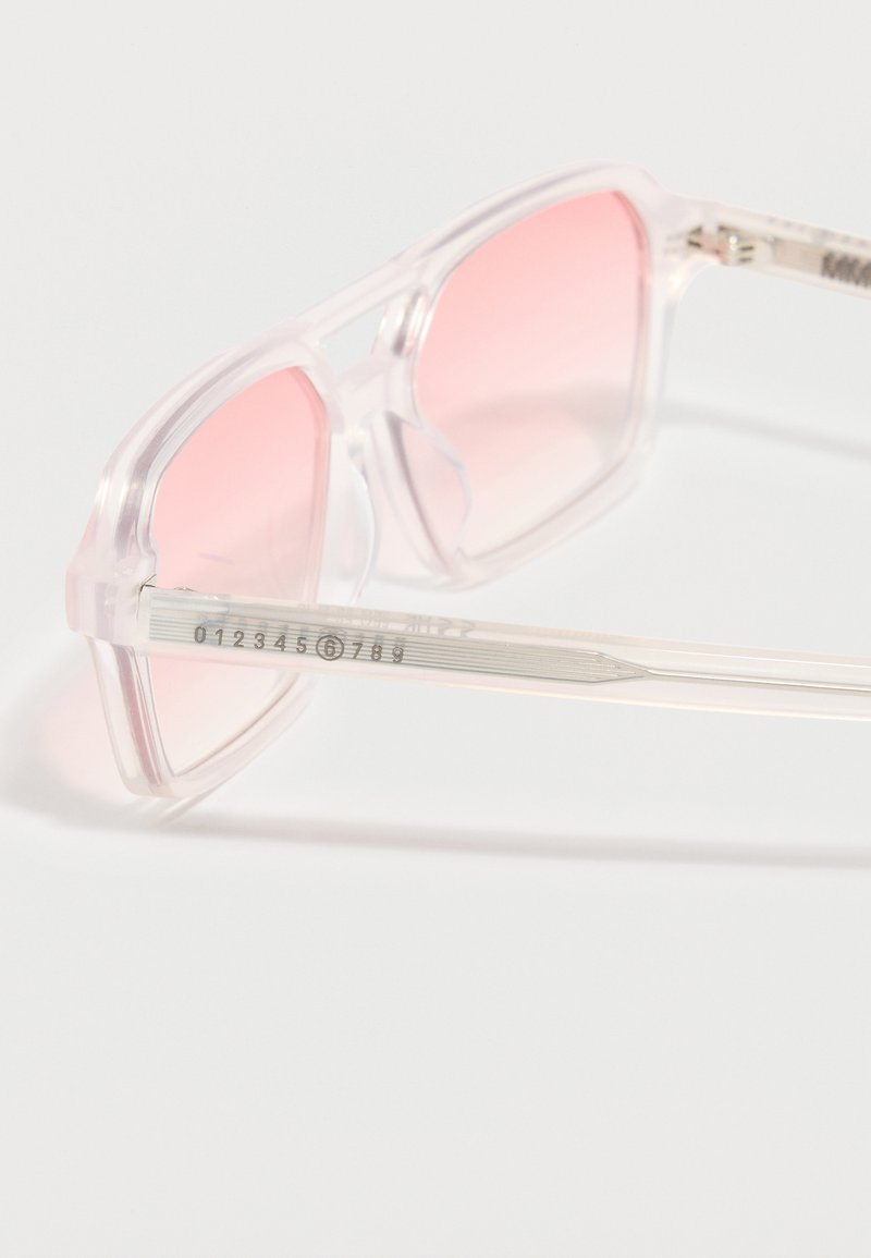 Lunettes de soleil carrées à monture transparente avec des verres dégradés roses translucides et des branches transparentes affichant des marquages numérotés.