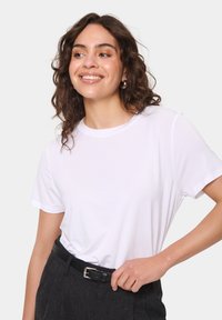 Tricou alb cu mânecă scurtă și guler rotund, prezentat împreună cu pantaloni închiși la culoare și o curea neagră. Material neted cu un design simplu.