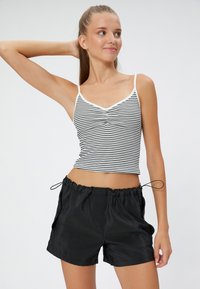 Top sin mangas a rayas en blanco y negro con escote en V y tirantes cortos, combinado con pantalones cortos negros de cintura elástica con bolsillos laterales y cordón.