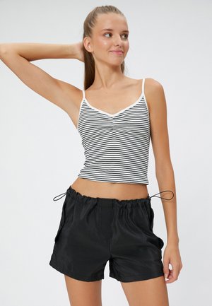 Schwarz-weiß gestreifes Tanktop mit V-Ausschnitt und kurzen Trägern, kombiniert mit schwarzen Shorts mit elastischem Bund, seitlichen Taschen und Kordelzug.