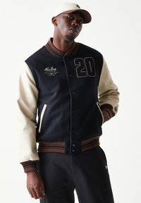 Λιβρέο μπουφάν σε ναυτικό μπλε και κρεμ χρώμα με ριγέ ριμπ ύφασμα στον γιακά, κεντημένο λογότυπο και τον αριθμό '20' στο μπροστινό μέρος, με κουμπιά τύπου κλιπ και πλαϊνές τσέπες.