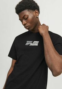 Melnas kokvilnas T-krekls ar centrālo pelēko logotipu un uzrakstu "JACK & JONES". Klasiska apļa apkakle un īsām piedurknēm. Gluda tekstūra.