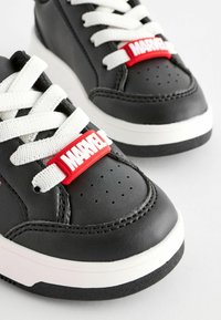 Baskets noires en cuir avec des lacets blancs et une étiquette en caoutchouc rouge portant "MARVEL". Équipées de détails perforés sur l'avant.