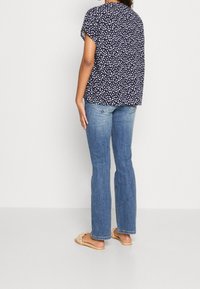 Top floral de manga corta en color navy, de corte holgado, mezcla de algodón. Combinado con jeans acampanados de color azul claro y sandalias planas de tejido, visto desde la parte de atrás.