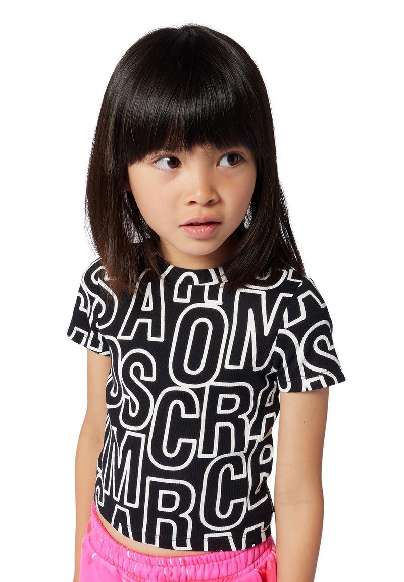 T-shirt noir court avec des impressions en lettres blanches audacieuses, des manches courtes et une texture côtelée. Associé à un short avec une ceinture élastique rose.