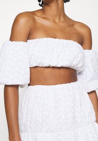 Top corto blanco sin mangas con mangas abullonadas, con patrones florales texturizados y fruncido elástico, combinado con una falda a juego.
