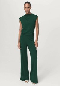 Mono verde oscuro con un cuello alto, diseño sin mangas y pantalones de pierna ancha, confeccionado en una suave tela que presenta un ajuste relajado.