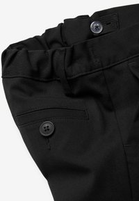 Schwarze Hose aus strukturiertem Stoff mit elastischem Bund, Knopfverschluss und einer Seitentasche mit dekorativem Knopfdetail.