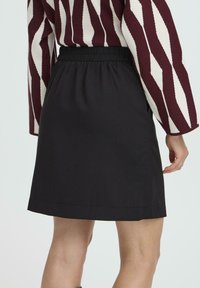 Mujer vestida con una falda negra de cintura elástica y un suéter de manga larga con rayas verticales en burdeos y blanco, vista desde atrás.