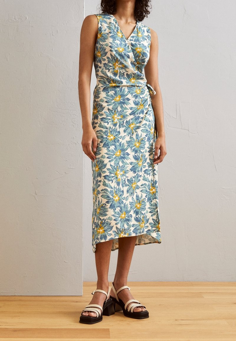 Kukkakuosiset kietaisumekko, jossa on sinisiä ja keltaisia kuvioita kermanvärisellä taustalla, korkea helma ja sivusolmu. Yhdistettynä kahden sävyn sandaaleihin.