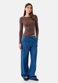 Brun, ribbet langærmet top sat sammen med løse, blå denimbukser med elastisk talje. Stylede med mørkebrune slip-on sko.