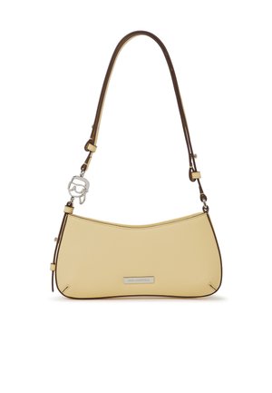 Mała beżowa torebka na ramię z cienkim brązowym paskiem, srebrną tabliczką z logo i ozdobnym srebrnym breloczkiem przymocowanym do pętli paska.