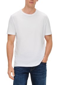 Weißes Baumwoll-T-Shirt mit Rundhalsausschnitt und kurzen Ärmeln, getragen von einer Person mit Händen in den Taschen, kombiniert mit blauen Jeans.