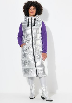 Lang zilveren puffer vest met een capuchon, voorzien van horizontale stiksels, sluiting met rits aan de voorkant en zwarte accenten. Gecombineerd met metallic leggings en laarzen.