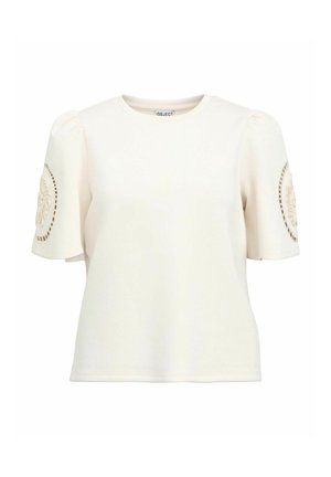 Cream-colored short-sleeve top with puffed sleeves, featuring a circular textured pattern on the left sleeve and a round neckline.