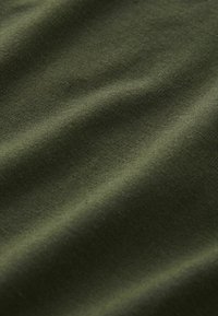 Dunkel olivgrüner Stoff in Nahaufnahme, zeigt feine Strickstruktur und weiche Falten unter diffusem Licht.