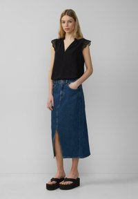 Černý top bez rukávů s krajkovým lemováním, v kombinaci s džínsovou sukní se předním rozparkem. Modelka na sobě má platformové sandály.
